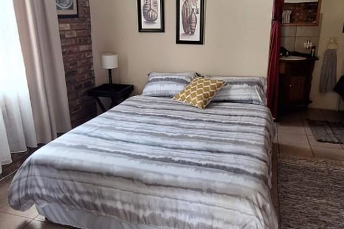 A bedroom featuring tiled flooring, a brick accent wall, and an open-plan layout leading to an en-suite bathroom area.