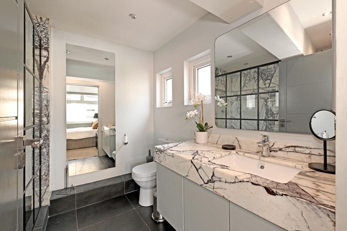 Modern bathroom featuring a marble vanity countertop, integrated basin, large wall mirror, and a walk-in shower with a black metal frame.