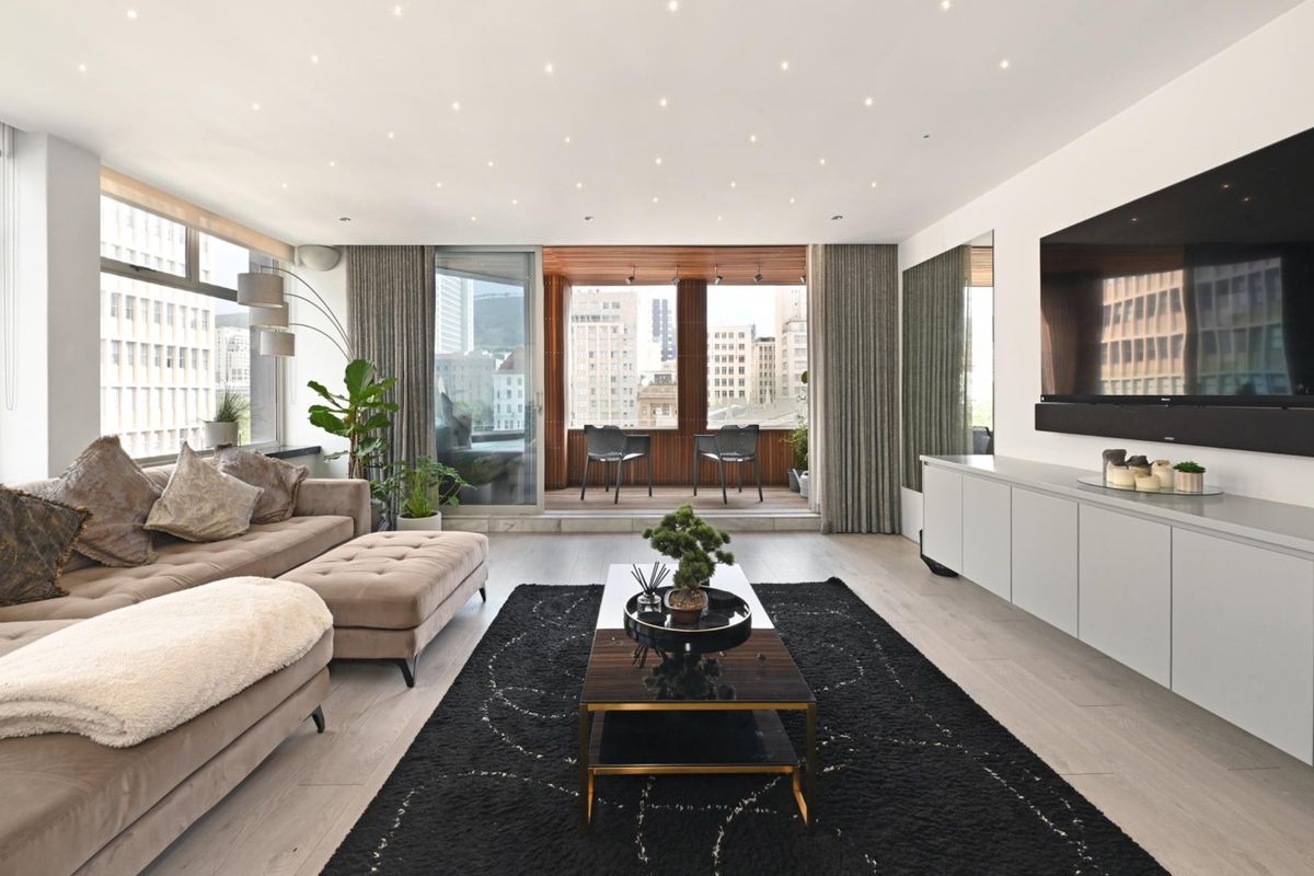 Modern open-plan living area featuring recessed ceiling lighting, light wood-look flooring, and seamless access to a private balcony with city views.