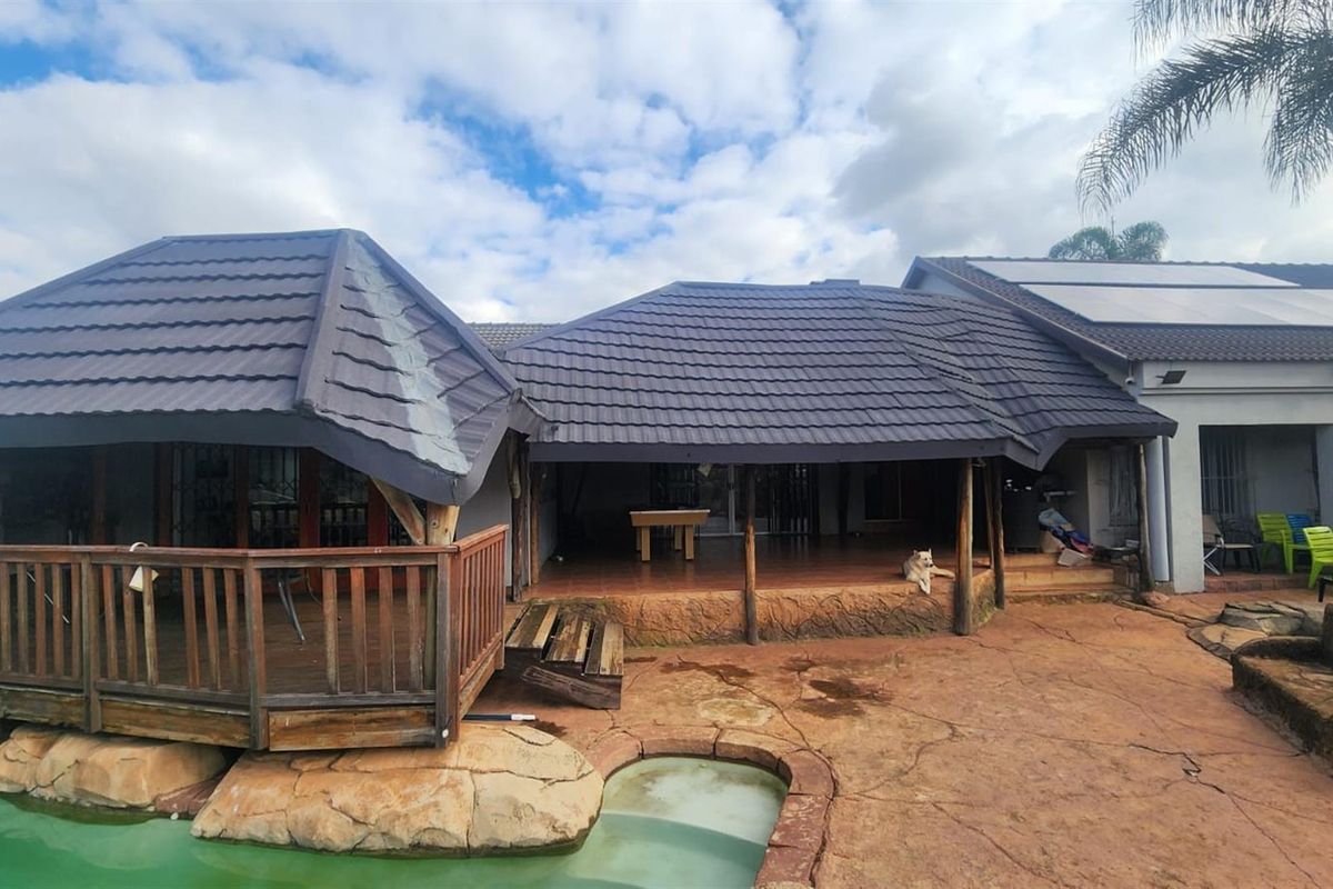 Rear exterior view featuring a covered patio, timber decking, and a swimming pool with natural rock features and solar panels on the roof.