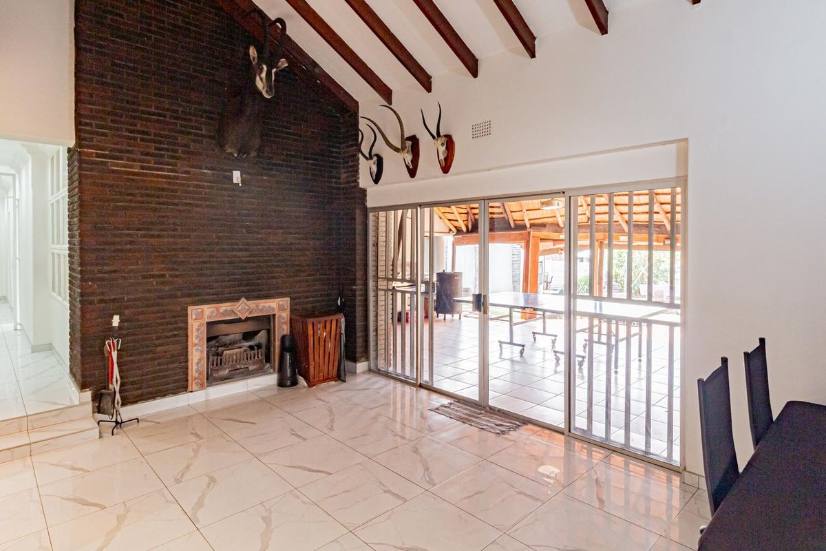 Spacious living area featuring a prominent dark brick fireplace, exposed timber ceiling beams, polished marble-look floor tiles, and sliding glass doors leading to the patio.