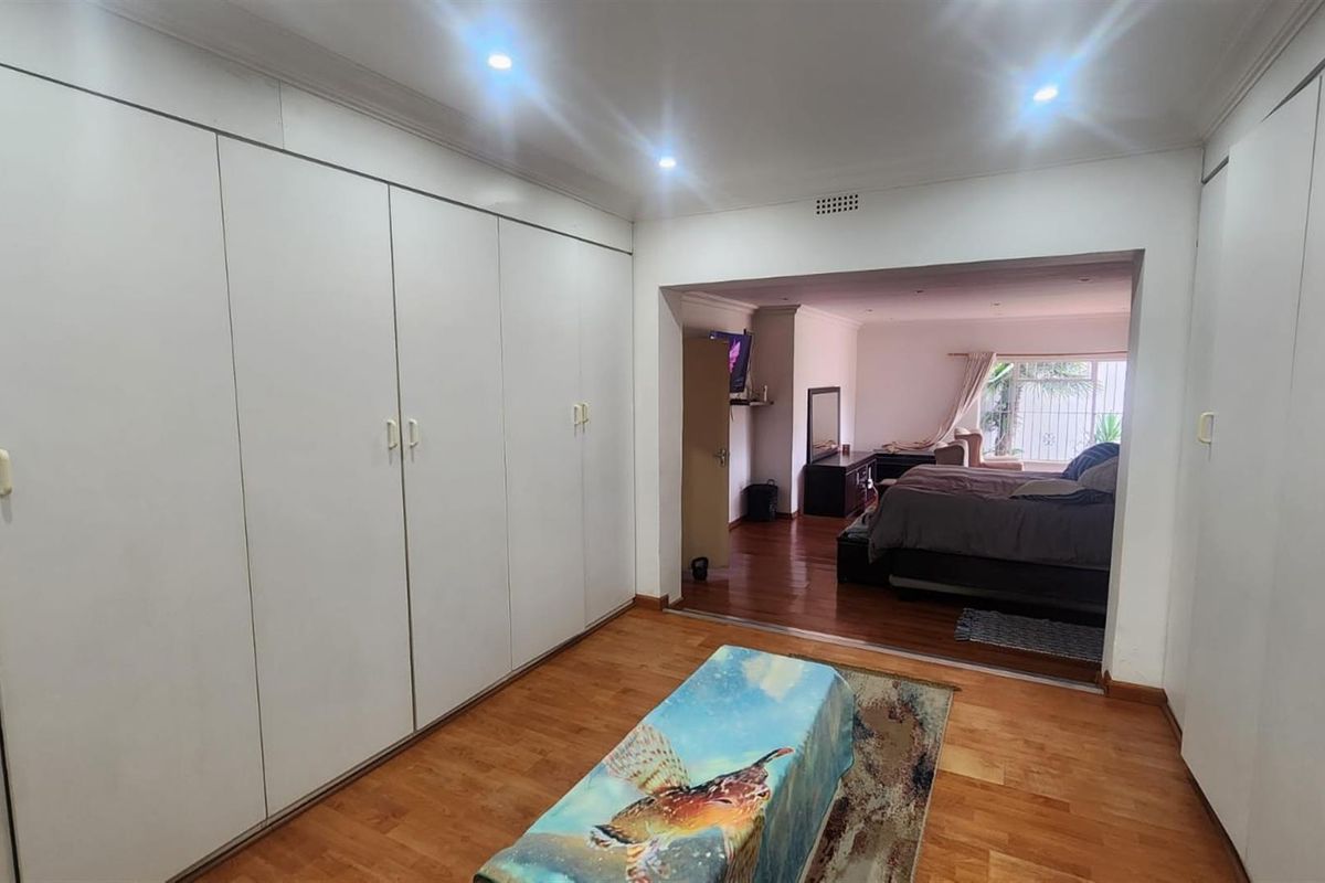 Spacious bedroom featuring extensive built-in cabinetry, recessed lighting, and warm wood-look flooring, leading into an adjoining living area.