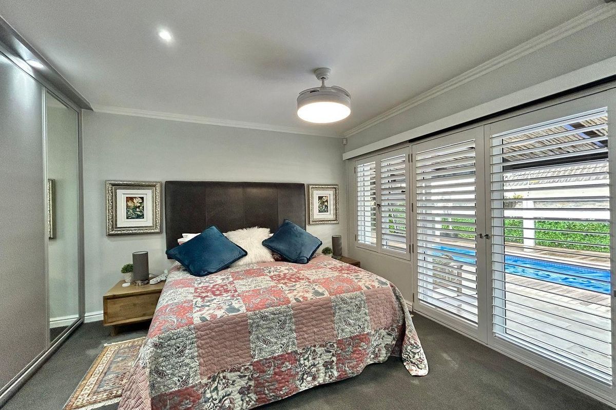 Spacious bedroom featuring built-in mirrored wardrobes, ceiling fan, and plantation shutters opening directly onto a private pool area.