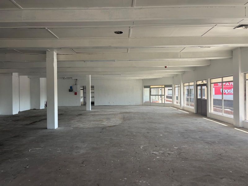 A spacious, open-plan retail unit featuring high ceilings with exposed beams, large windows for natural light, and a raw concrete floor finish.