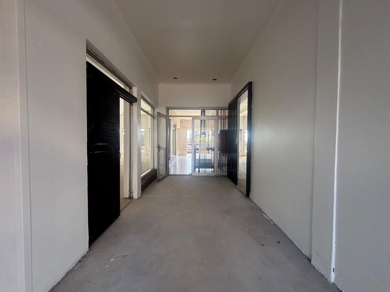A vacant commercial hallway featuring neutral walls, recessed lighting, and access through glass doors and a security gate.