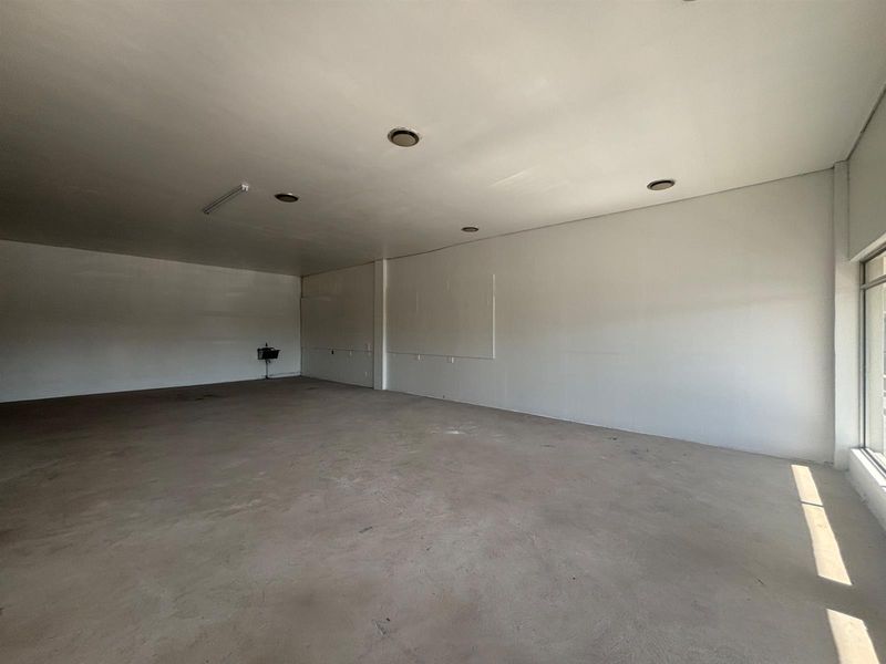 A spacious, vacant retail unit featuring concrete flooring, recessed ceiling lighting, and a large glass storefront window, offering a blank canvas for customization.