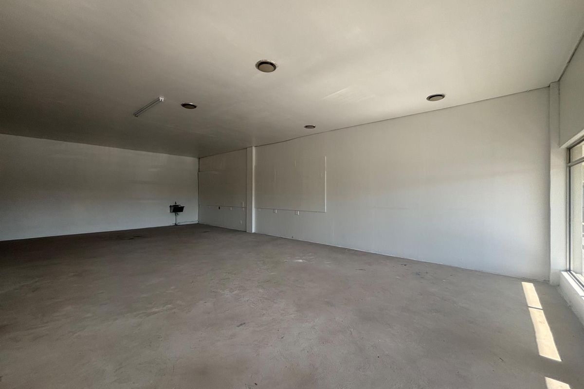 A spacious, vacant retail unit featuring concrete flooring, recessed ceiling lighting, and a large glass storefront window, offering a blank canvas for customization.
