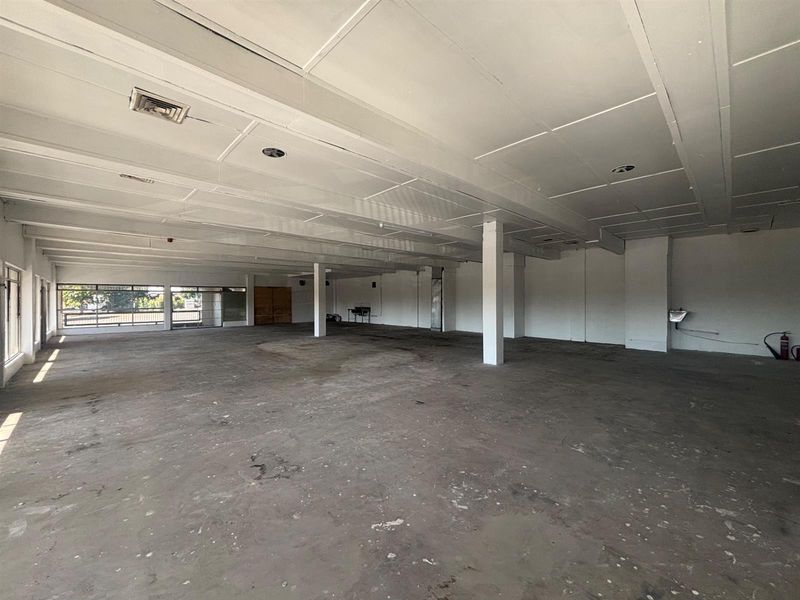 A large, open-plan retail space featuring exposed ceiling beams, support columns, and expansive windows, currently in a shell condition ready for fit-out.