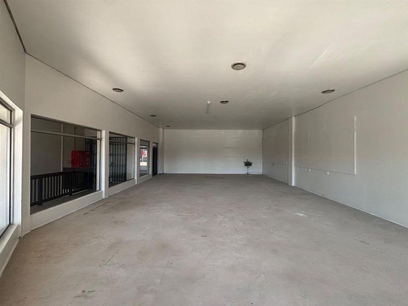 A spacious, empty retail unit featuring large display windows, recessed downlights, and concrete flooring, offering a blank canvas for various commercial business applications.