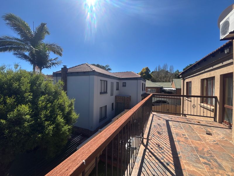 An elevated balcony featuring tiled flooring and a metal balustrade with a wooden handrail, overlooking the surrounding property grounds.