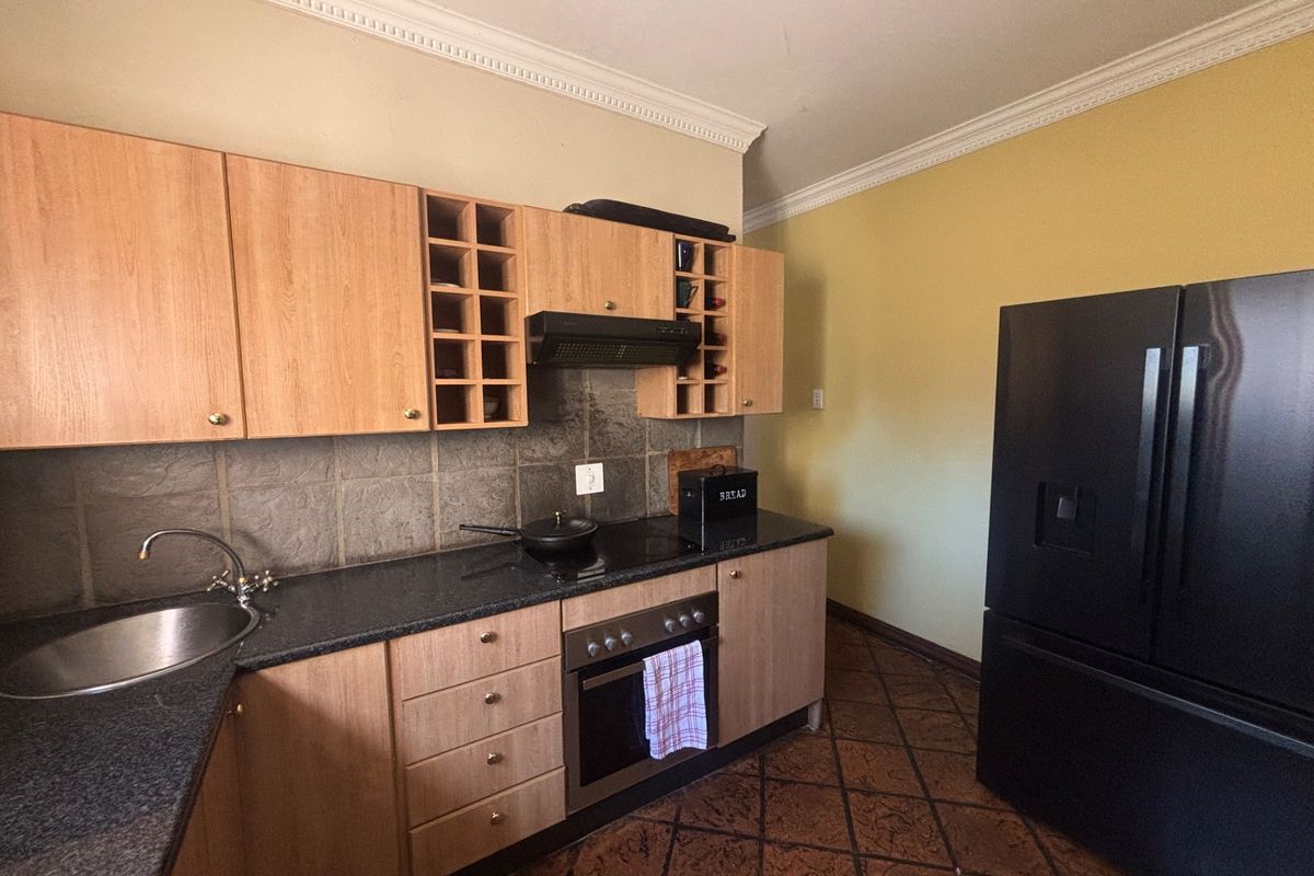 Functional kitchen featuring light wood cabinetry, granite countertops, built-in oven, hob, and extractor fan, complemented by tiled flooring and decorative cornice detailing.