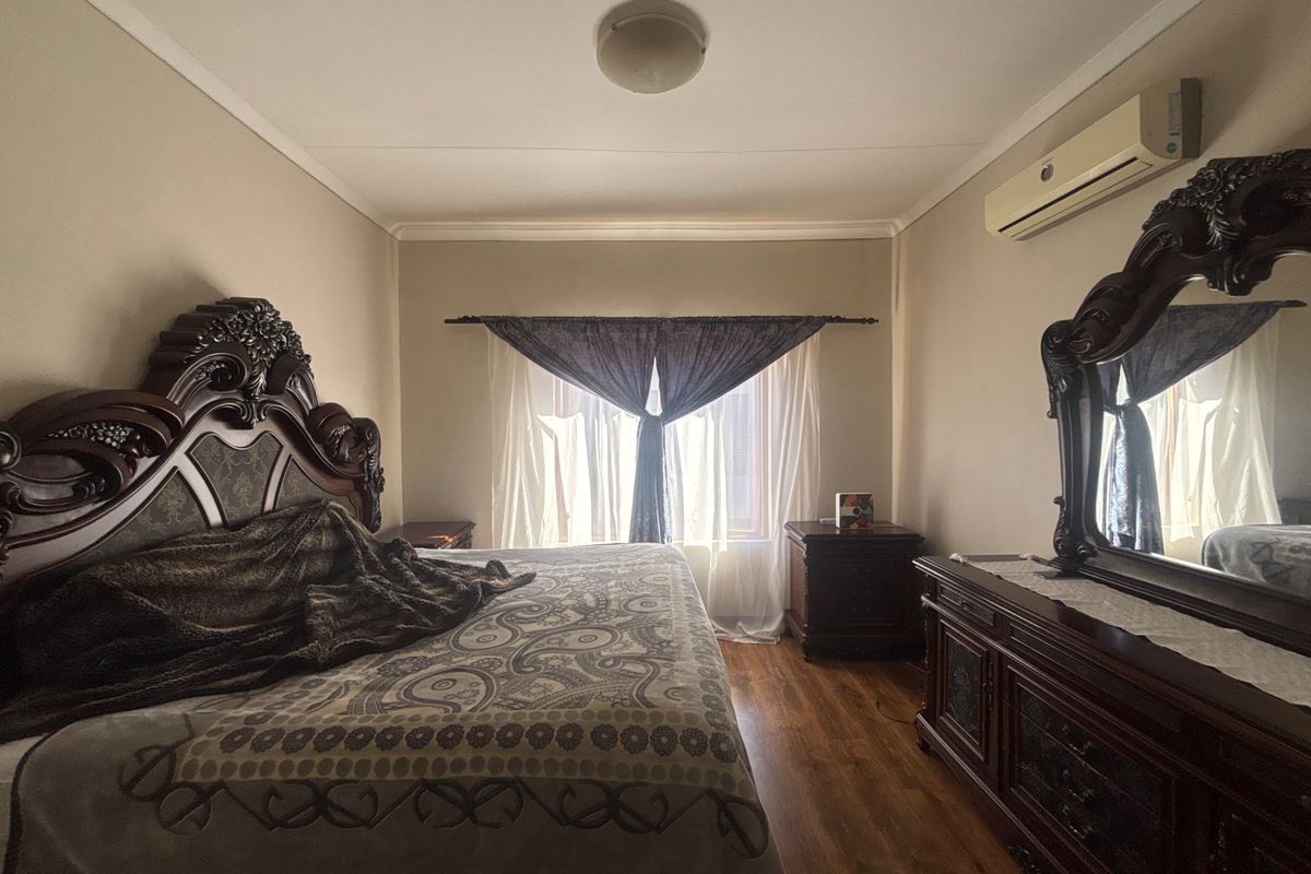 A bedroom featuring laminate flooring, a wall-mounted split-system air conditioner, and a central ceiling light fixture.