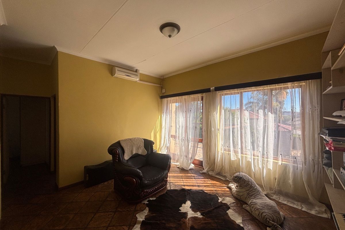 A living room featuring tiled flooring, a wall-mounted air conditioning unit, and built-in shelving, with access to an outdoor area through sliding glass doors.