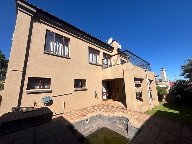 Rear view of the property featuring a tiled patio, a balcony with wrought iron railings, and a swimming pool requiring maintenance.