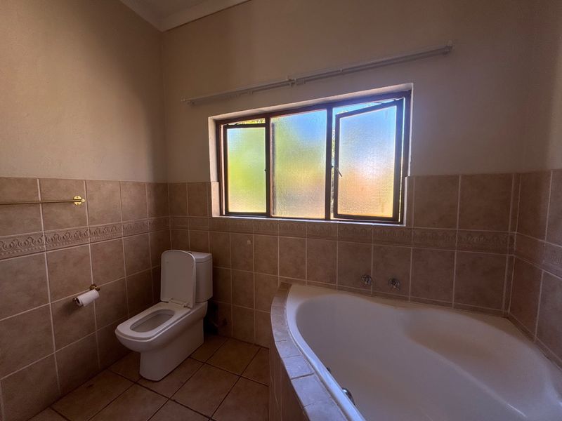 A functional bathroom featuring a built-in corner bathtub, toilet, and neutral tiled finishes, offering a blank canvas for potential modernization.