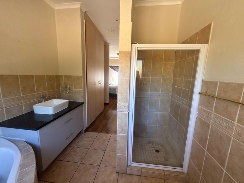A functional bathroom featuring a modern vessel sink vanity, a separate shower enclosure, and built-in storage cupboards with neutral tile finishes.