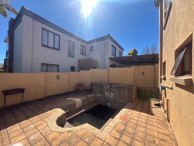 Rear courtyard featuring a built-in braai area and a swimming pool, enclosed by high boundary walls.