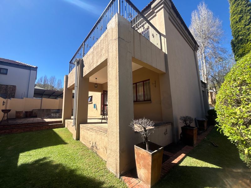 Rear view of the property featuring a covered patio, an upper-level balcony with wrought iron railings, and a private garden with a built-in braai area.
