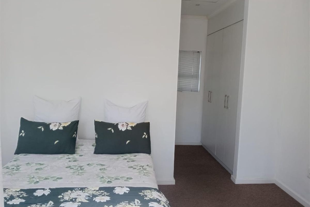 A bedroom featuring built-in cupboards and a window with venetian blinds, finished with neutral walls and carpeted flooring.