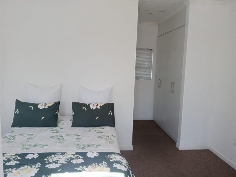 A bedroom featuring built-in cupboards and a window with venetian blinds, finished with neutral walls and carpeted flooring.