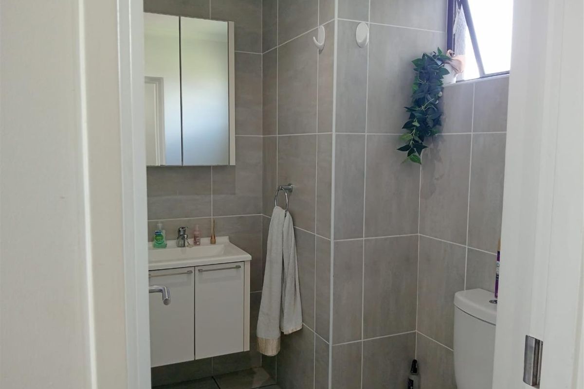 A compact, modern bathroom featuring grey wall tiles, a white vanity with basin, a mirrored medicine cabinet, and a standard toilet.