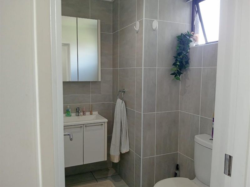 A compact, modern bathroom featuring grey wall tiles, a white vanity with basin, a mirrored medicine cabinet, and a standard toilet.