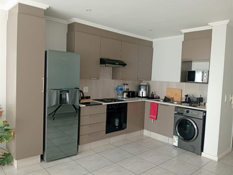 Modern kitchen featuring sleek taupe cabinetry, tiled flooring, integrated appliances, and a functional layout with a tiled backsplash and recessed lighting.