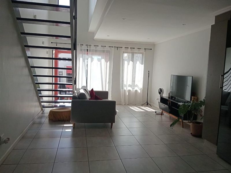Spacious open-plan living area featuring modern tiled flooring, an architectural open-tread staircase, and large sliding doors providing ample natural light.