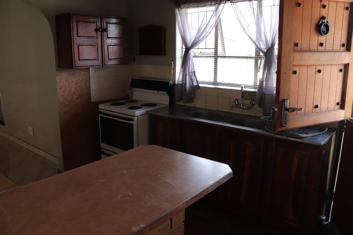 A dated kitchen featuring wooden cabinetry, a freestanding stove, and a double sink with a window view.