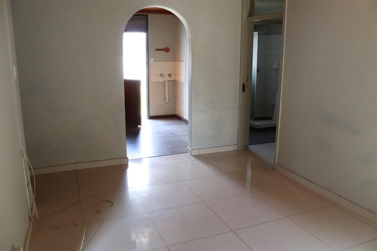 An empty interior space featuring tiled flooring, an arched doorway leading to a utility area, and an adjacent bathroom entrance.