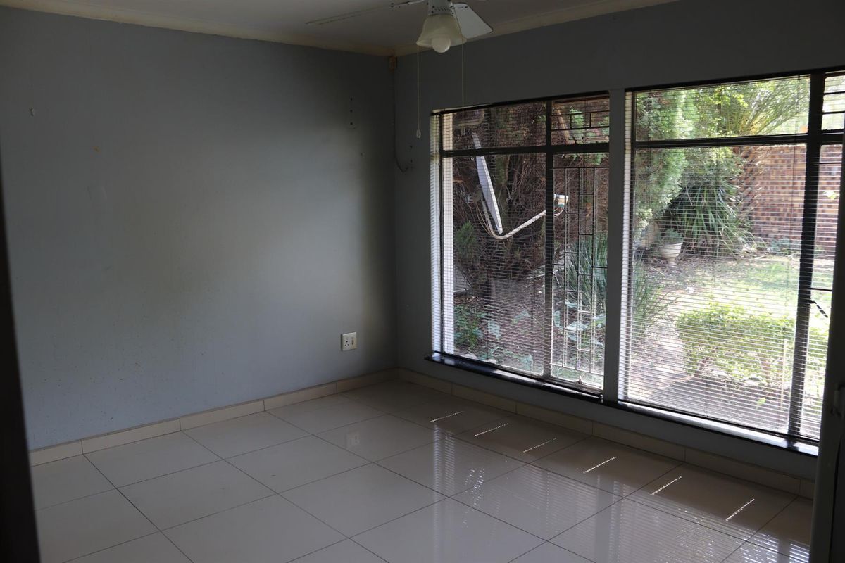 An empty bedroom featuring tiled flooring, a ceiling fan, and large windows with security bars overlooking the garden.