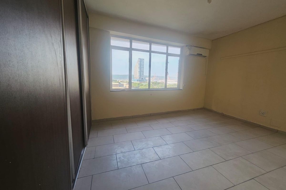An empty bedroom featuring tiled flooring, a built-in sliding wardrobe, and a split-system air conditioning unit with a view through the large window.