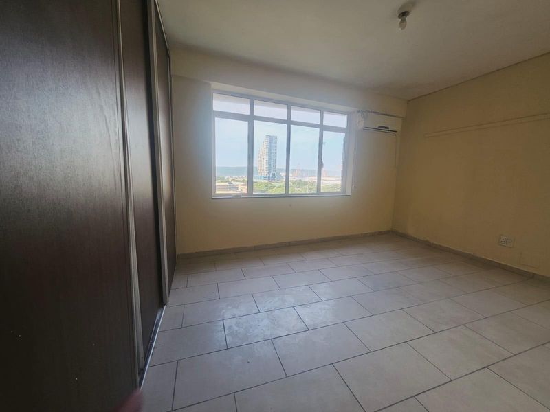 An empty bedroom featuring tiled flooring, a built-in sliding wardrobe, and a split-system air conditioning unit with a view through the large window.