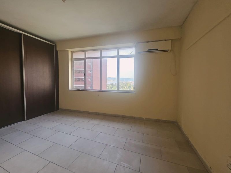 An empty bedroom featuring tiled flooring, a built-in sliding wardrobe, and a wall-mounted air conditioning unit with natural light from a large window.