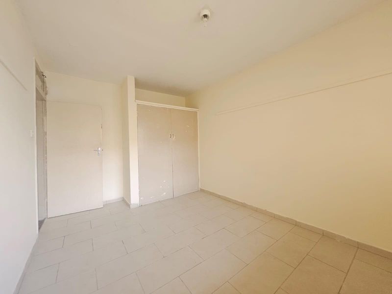 An empty bedroom featuring tiled flooring and a built-in cupboard, offering a blank canvas for potential renovation or interior design updates.