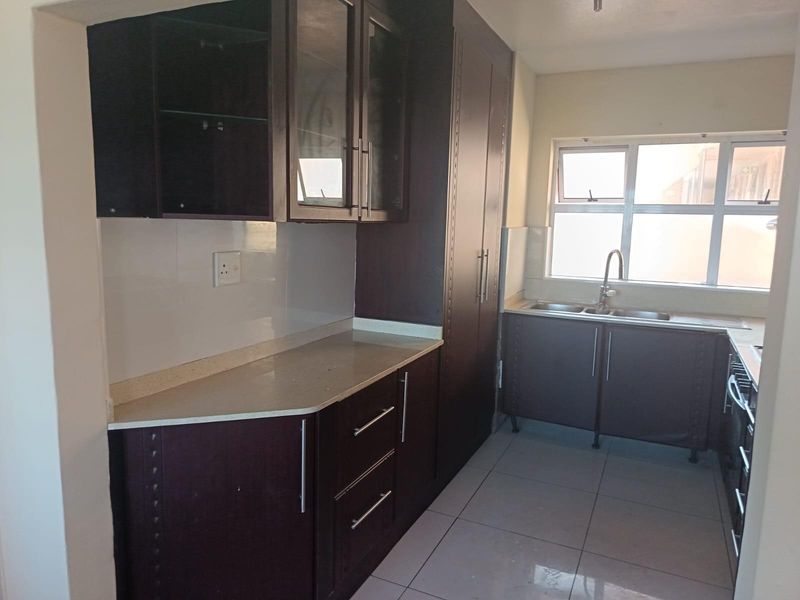 A functional kitchen featuring dark wood cabinetry, stone countertops, a double basin sink, and tiled flooring, offering ample storage and workspace.