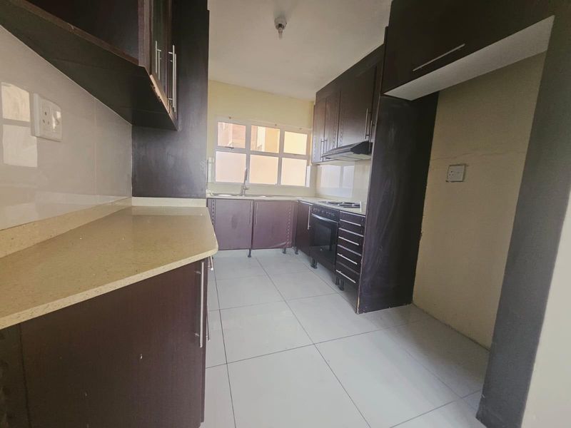 A functional kitchen featuring dark wood cabinetry, stone countertops, built-in oven, extractor fan, and tiled flooring in a clean, empty space.