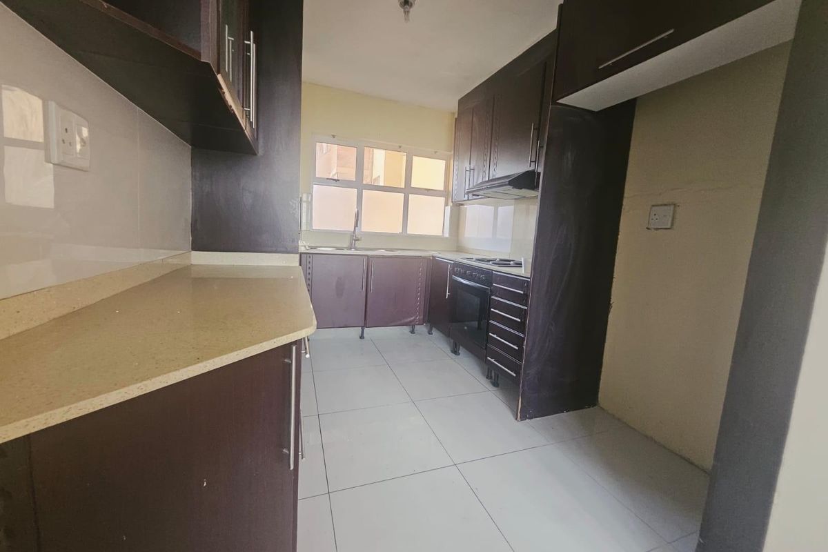 A functional kitchen featuring dark wood cabinetry, stone countertops, built-in oven, extractor fan, and tiled flooring in a clean, empty space.