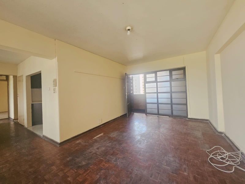 Spacious living area featuring original parquet flooring and a large sliding glass door leading to an outdoor space, offering a blank canvas for renovation.