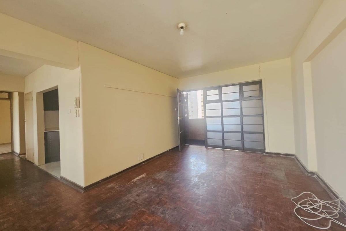 Spacious living area featuring original parquet flooring and a large sliding glass door leading to an outdoor space, offering a blank canvas for renovation.
