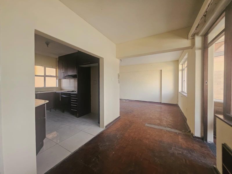 Open-plan living area featuring parquet flooring and an adjoining kitchen with built-in cabinetry, hob, and oven, offering a blank canvas for renovation.