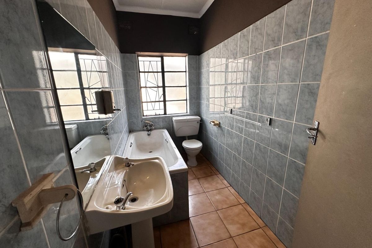 A dated bathroom featuring a bathtub, pedestal basin, and toilet with blue wall tiling and brown floor tiles.