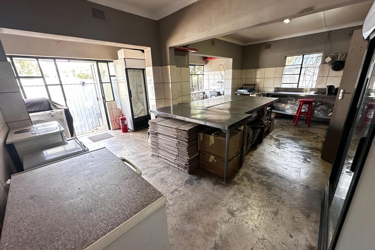A functional commercial-style kitchen space featuring stainless steel prep surfaces, tiled splashbacks, and direct access to the exterior.