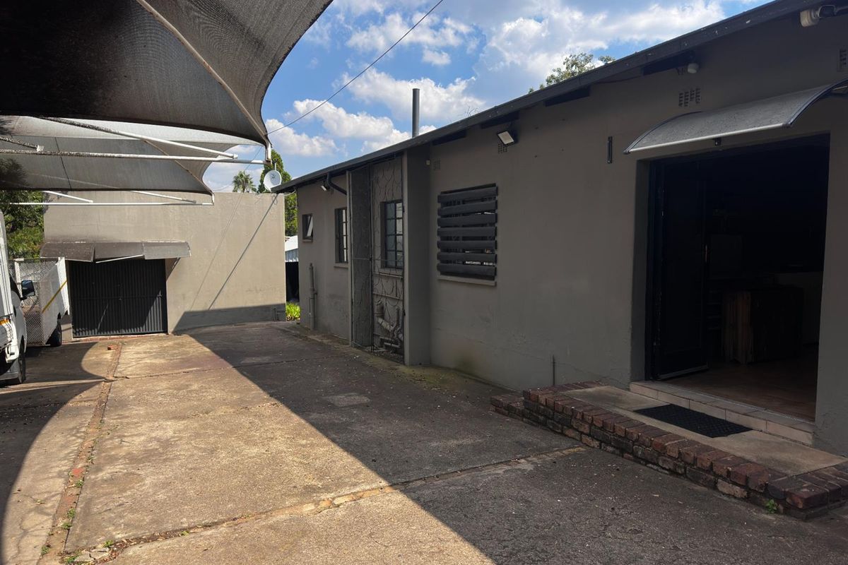 Rear exterior view showing a concrete driveway, shade sail structure, and access to the main building with brick step detailing.