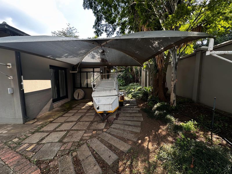 A paved outdoor patio area featuring a large shade sail, providing a functional space for outdoor storage or potential entertainment area.