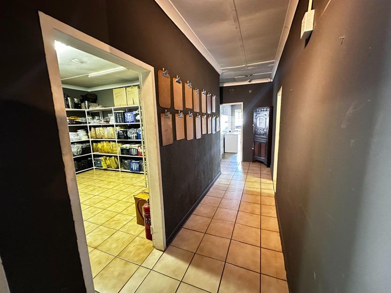 A functional hallway with tiled flooring leading to a storage area with built-in shelving and a secondary utility space.