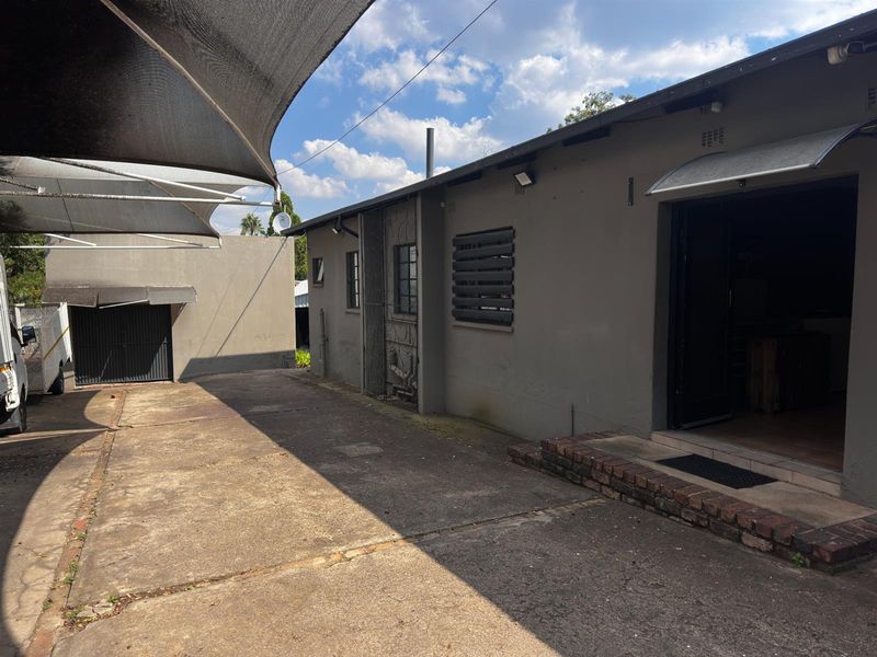 Rear exterior view showing a concrete driveway, shade sail structure, and access to the main building with brick step detailing.