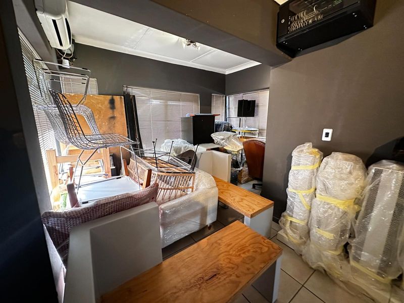 A living area featuring tiled flooring, venetian blinds, and a wall-mounted air conditioning unit, currently used for storage.