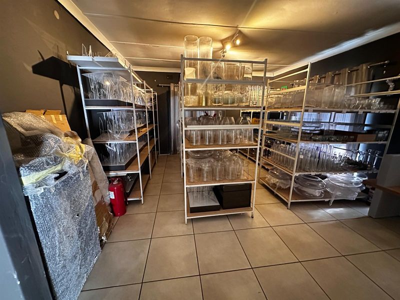 A functional utility or storage space featuring tiled flooring, ceiling-mounted track lighting, and a wall-mounted fire extinguisher.