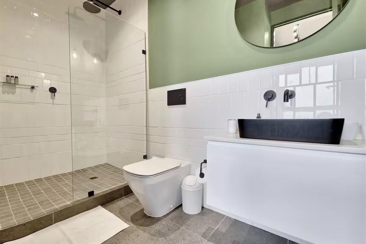 Modern bathroom featuring a walk-in glass shower, wall-mounted toilet, and a sleek vanity with a black vessel sink and matte black fixtures.